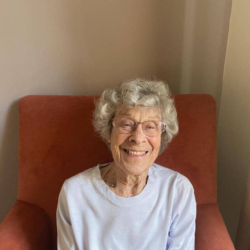 Jean, resident at Juniper House Care Home in Worcester, sits in a chair and smiles.